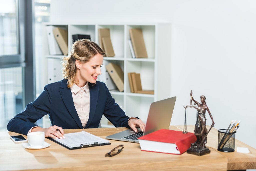 portrait of smiling lawyer working on laptop at workplace with documents and cup of coffee in office